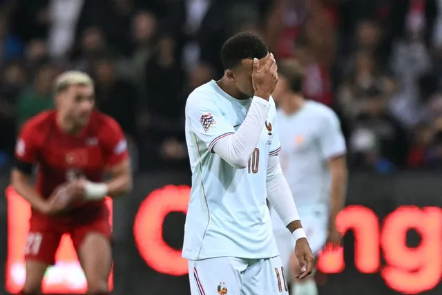 Un jucător de fotbal în echipament alb cu numărul zece își acoperă fața cu mâna, în timp ce alți doi jucători sunt vizibili în fundal.
