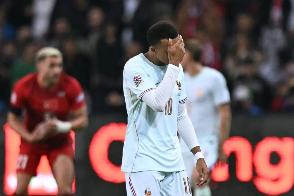 Un jucător de fotbal în echipament alb cu numărul zece își acoperă fața cu mâna, în timp ce alți doi jucători sunt vizibili în fundal.