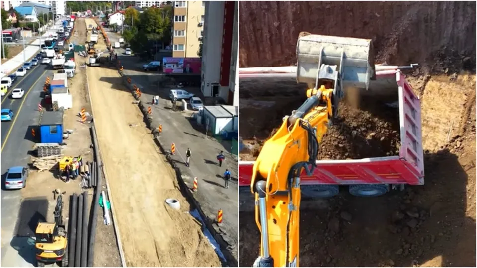 O excavatoare galbenă încarcă pământ într-un camion roșu, în timp ce în partea stângă se observă un șantier cu utilaje și mașini pe un drum.