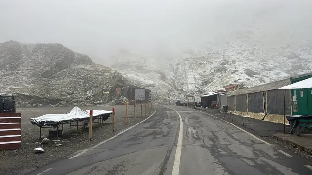 Un drum asfaltat cu linii albe traversează un peisaj montan acoperit de zăpadă sub un cer înnorat și brumat.