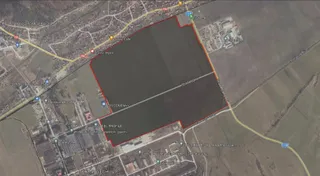 O vedere aeriană de satelit prezintă un teren mare, delimitat cu o linie roșie, situat lângă drumuri și clădiri industriale.
