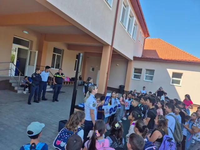 Un grup de copii stă în fața unei clădiri lângă doi polițiști care stau în picioare lângă un panou informativ.