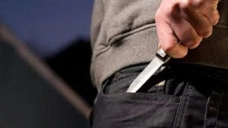 O persoană poartă un obiect metalic tăietor în buzunarul unei pantaloni negri.