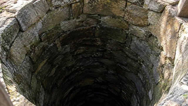 O privire de sus asupra unei fântâni circulare cu pereți construiți din pietre gri suprapuse.