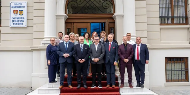 Un grup de oameni în haine formale stă în rând în fața unei intrări de clădire cu coloane albe.