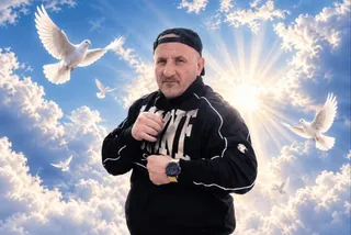 Un bărbat cu șapcă și haine negre stă în fața unui cer albastru cu nori și păsări albe în zbor.