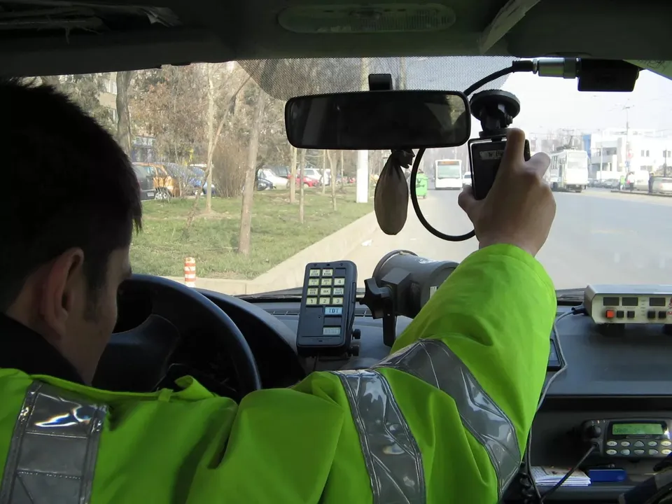 Un bărbat cu o jachetă verde fluorescente ține un aparat de măsurare în interiorul unui vehicul, orientat spre parbriz.
