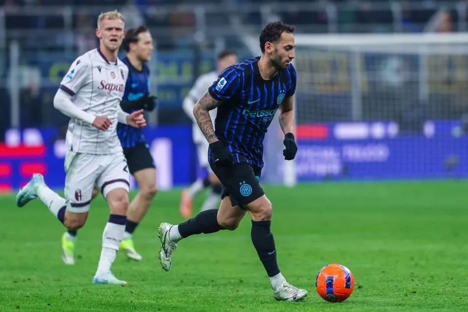 Un fotbalist într-un echipament alb și negru aleargă pe terenul de fotbal lângă un balon portocaliu și alb.