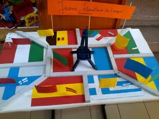 O machetă pe o masă reprezintă steaguri naționale europene și un model al Turnului Eiffel, sugerând o activitate școlară legată de diversitatea lingvistică europeană.