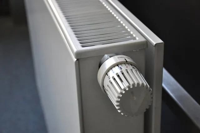 Un radiator alb cu un termostat rotativ setat pe o scară numerică este montat pe un perete gri.