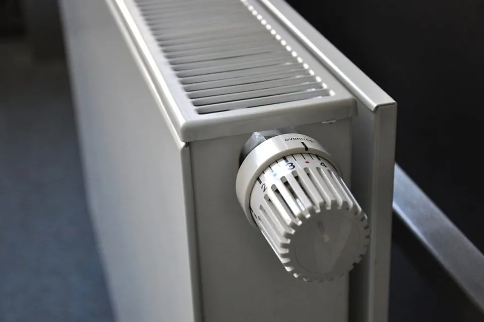 Un radiator alb cu un termostat rotativ setat pe o scară numerică este montat pe un perete gri.