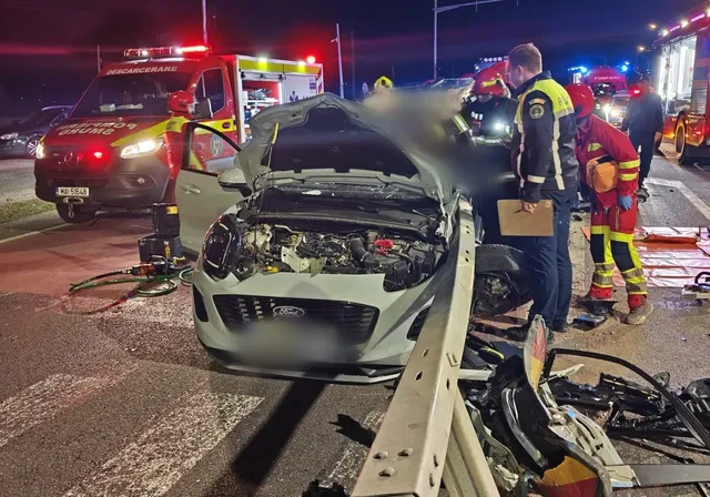 O mașină albă cu capota deschisă stă pe drum lângă un vehicul de intervenție și persoane îmbrăcate în uniforme de serviciu.