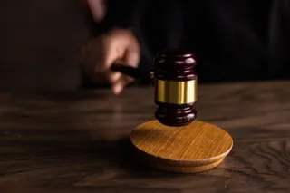 O mână ține un ciocan de lemn cu un inel metalic așezat pe o suprafață de lemn întunecată.