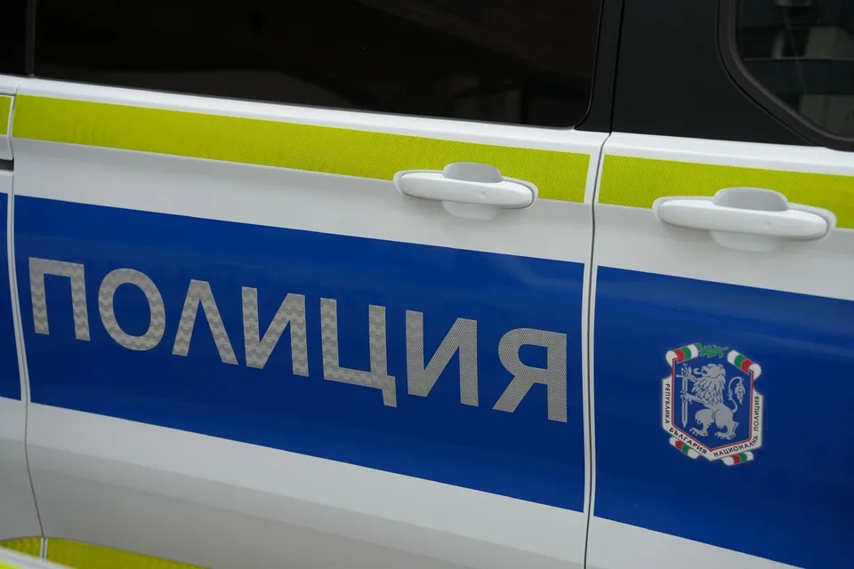 Un autovehicul alb cu o bandă albastră pe care scrie textul scris în alfabet chirilic și un emblema colorată.