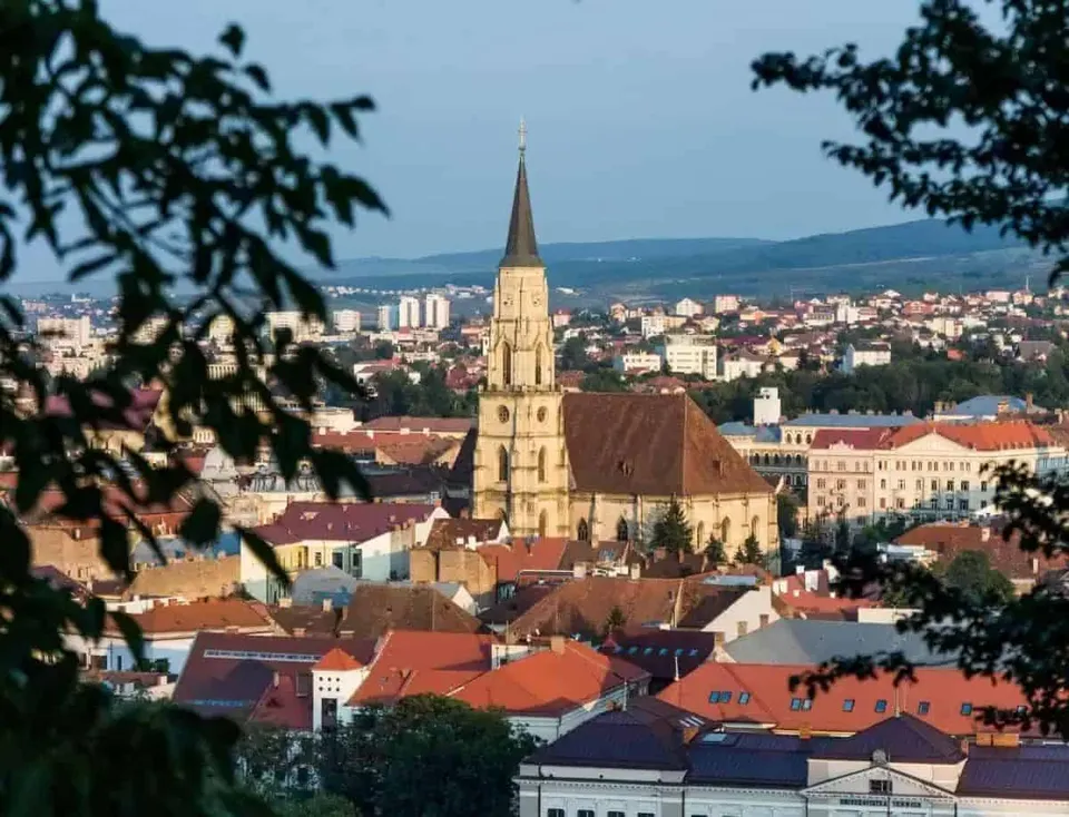 O catedrală cu un turn înalt și ascuțit domină un peisaj urban format din clădiri cu acoperișuri în nuanțe de roșu și portocaliu.