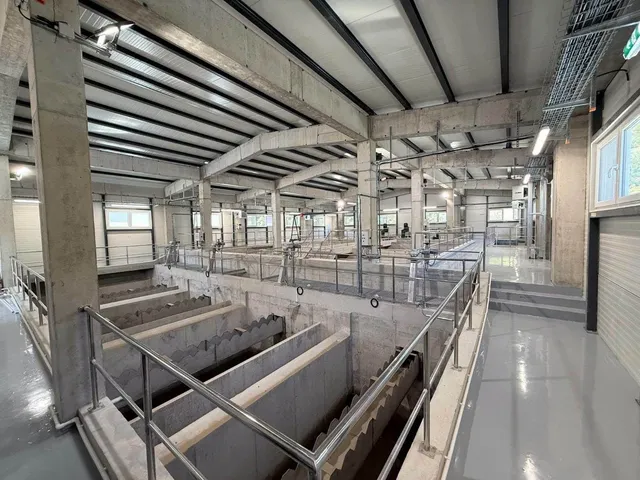Interiorul unei clădiri industriale cu structură de beton, containere de depozitare și balustrade metalice pe coridoare gri lucioase.