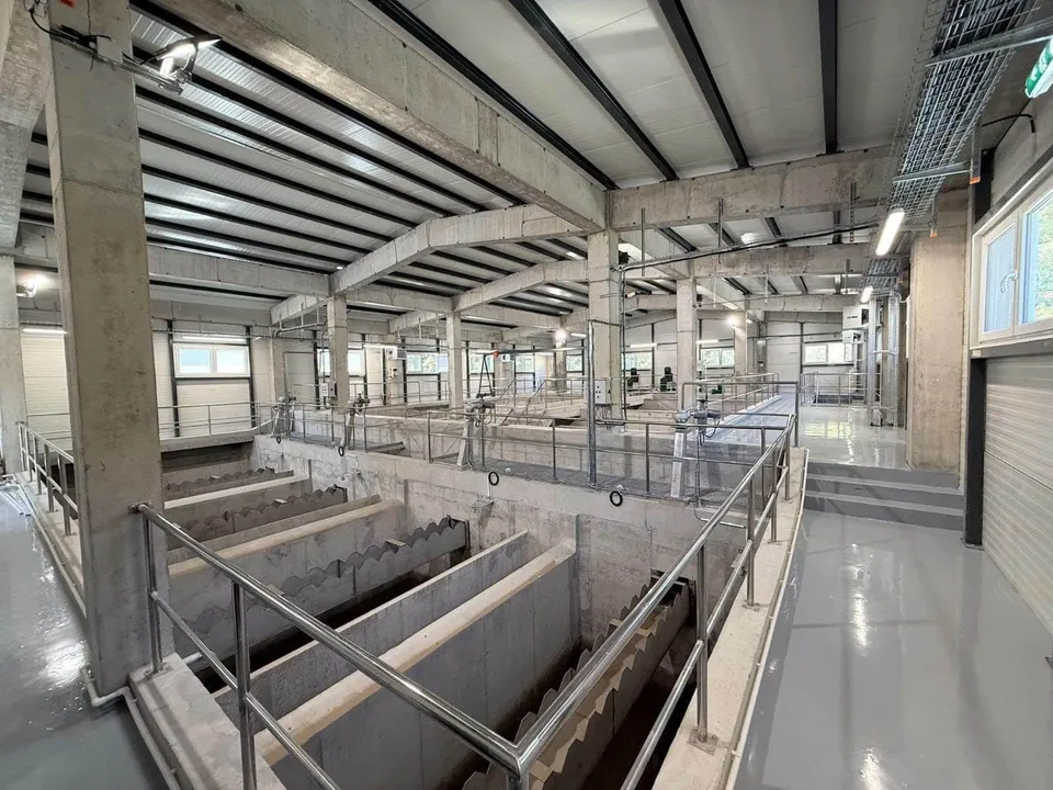 Interiorul unei clădiri industriale cu structură de beton, containere de depozitare și balustrade metalice pe coridoare gri lucioase.