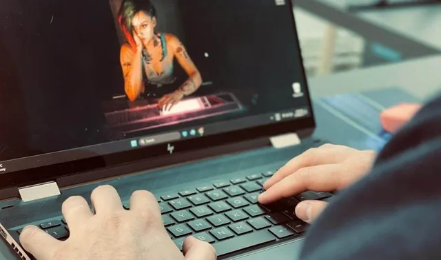 Mâinile unei persoane tastând pe un laptop deschis care afișează o imagine cu o femeie pe ecran.