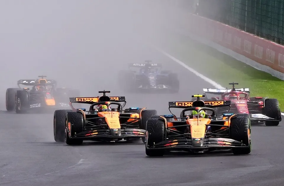 Patru mașini de Formula 1 circulă pe un circuit de curse în condiții de ceață densă și asfalt umed.