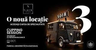 Un camion negru cu un panou publicitar NOIR este poziționat pe un fundal negru lângă un număr mare alb.