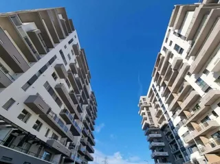 Două clădiri de apartamente moderne, înalte, cu balcoane, văzute din unghi jos spre cerul albastru.