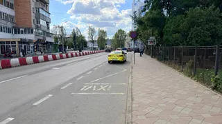 O mașină galbenă este parcată pe marginea unei străzi lângă un trotuar, lângă o marcaj rutier pe care scrie taxi.