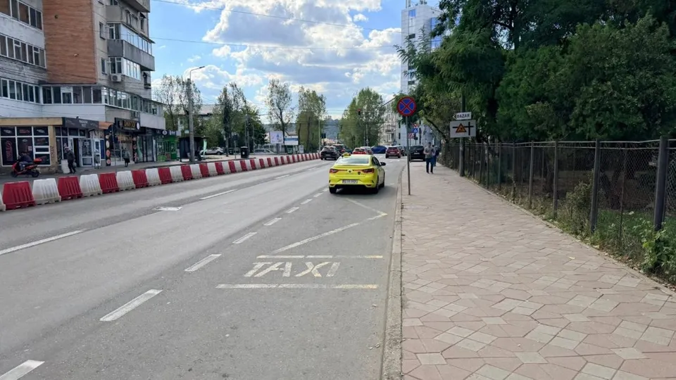 O mașină galbenă este parcată pe marginea unei străzi lângă un trotuar, lângă o marcaj rutier pe care scrie taxi.