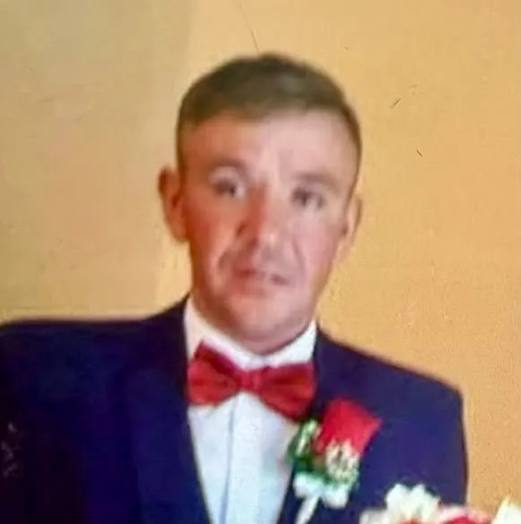 Un bărbat cu păr scurt și sacou închis, cămașă albă și papion roșu privește direct spre cameră.