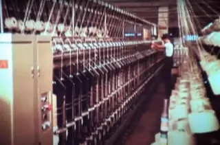 Un operator stă lângă un rând lung de utilaje industriale cu bobine albe dispuse pe o linie de producție într-o fabrică.