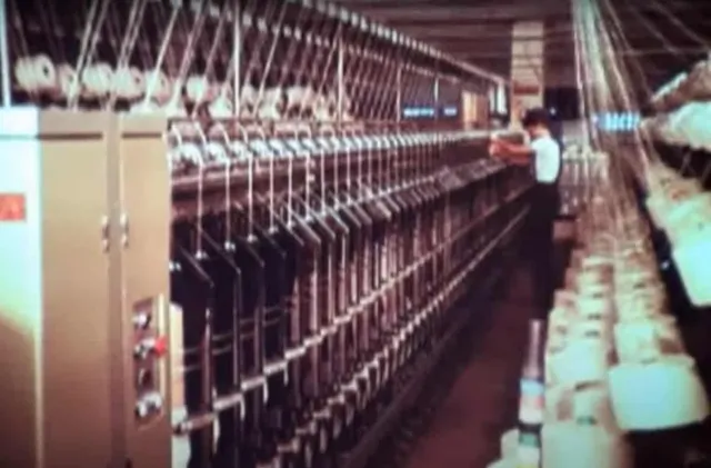 Un operator stă lângă un rând lung de utilaje industriale cu bobine albe dispuse pe o linie de producție într-o fabrică.