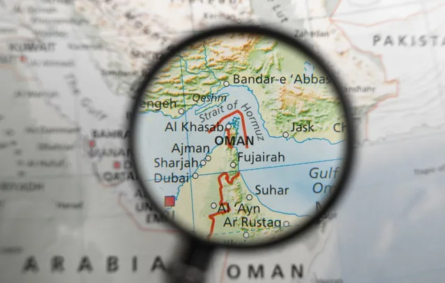 O lupă concentrează privirea asupra unei secțiuni dintr-o hartă care indică Strâmtoarea Ormuz și regiunea de lângă Oman.