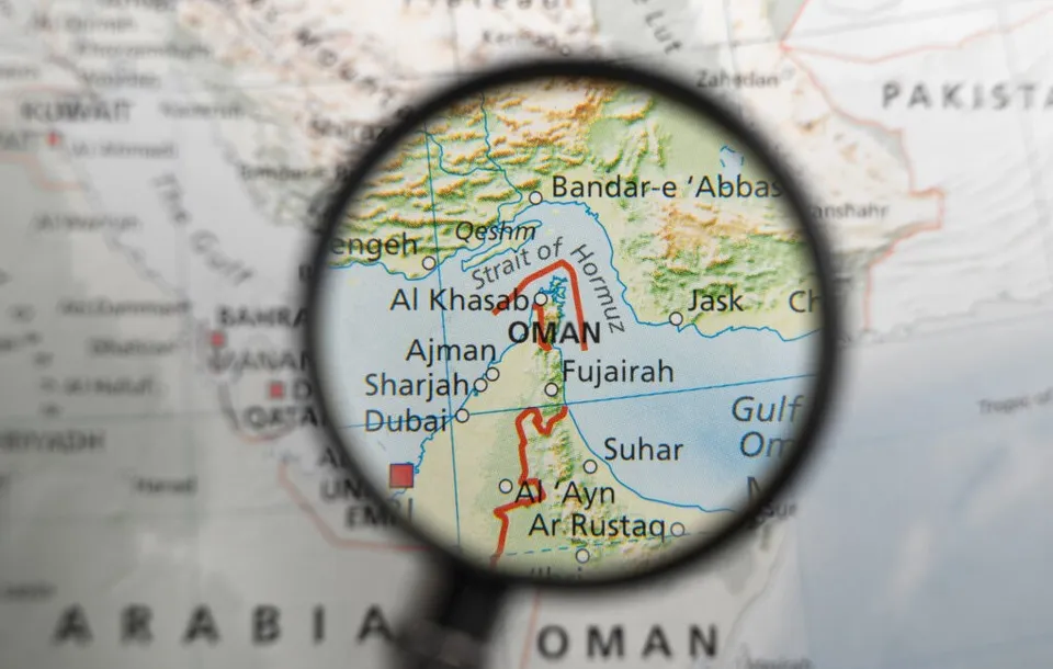 O lupă concentrează privirea asupra unei secțiuni dintr-o hartă care indică Strâmtoarea Ormuz și regiunea de lângă Oman.