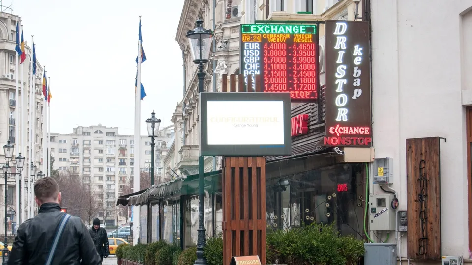 Un bărbat cu o geantă de umăr stă în fața unui restaurant care are un panou de schimb valutar și un afiș vertical cu textul Dristor Kebap.