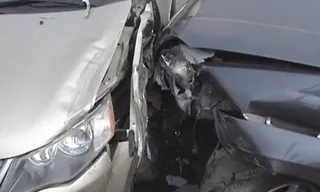 Două autoturisme de culoare deschisă și închisă prezintă daune structurale majore în zona frontală, fiind contactate direct.
