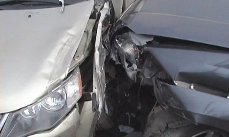 Două autoturisme de culoare deschisă și închisă prezintă daune structurale majore în zona frontală, fiind contactate direct.