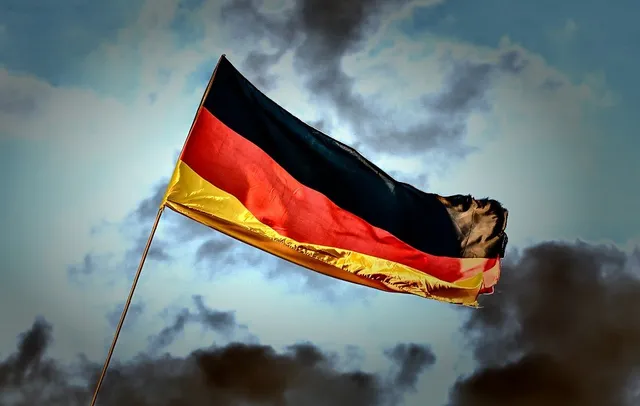 O steag german cu culorile negru, roșu și auriu flutură pe un stârp sub un cer înconjurat de nori întunecați.