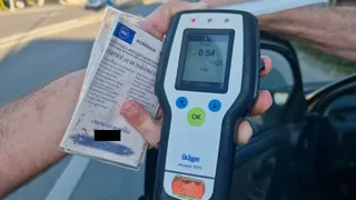 O persoană ține un aparat de testare a alcoolului cu afișajul digital și un certificat de înmatriculare într-o mână, lângă o mașină.