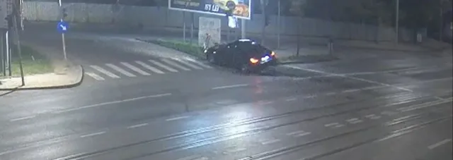 Un autoturism de culoare închisă este poziționat pe marginea unei străzi lângă un stâlp, sub lumina nocturnă.