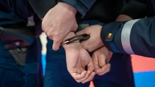 Mâinile unei persoane sunt prinse în cătușe de o persoană care poartă o uniformă în culori închise.