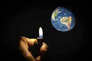 O mână ține o brichetă aprinsă în fața unei imagini a planetei Pământ pe un fundal negru.