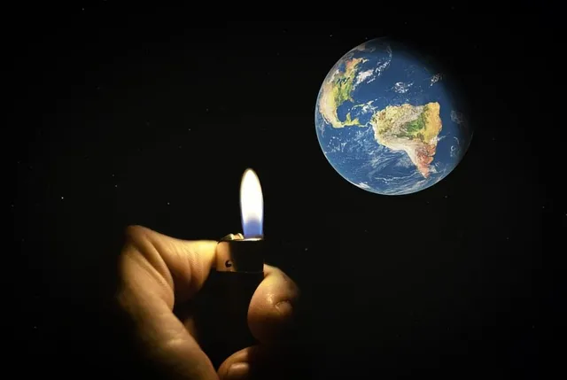 O mână ține o brichetă aprinsă în fața unei imagini a planetei Pământ pe un fundal negru.