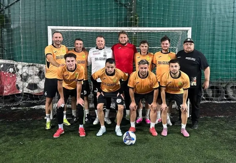 O echipă de șase bărbați în tricouri galbene și cinci bărbați în diverse tricouri stau în grup pe un teren de fotbal în fața unei porți.