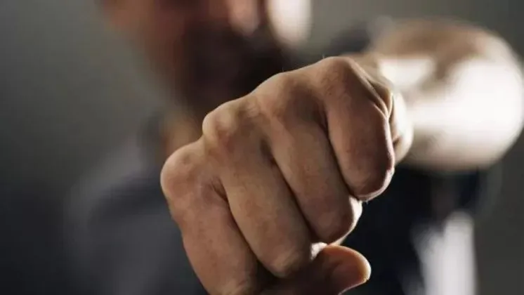 Un bărbat stă cu mâna închisă într-un pumn, poziționată în prim-plan, în fața unui fundal întunecat și neclar.