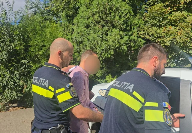 Unii polițiști în uniformă albastră și galbenă stau lângă un bărbat îmbrăcat într-un tricou roz lângă o mașină albă.